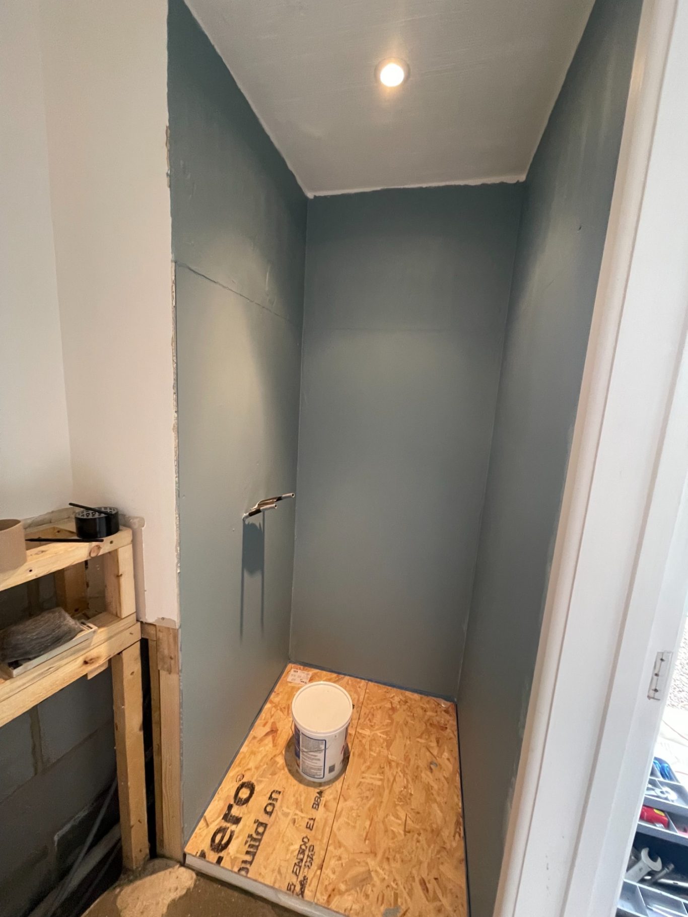 Shower enclosure waterproofed A small, unfinished shower area with blue walls and a wooden floor.