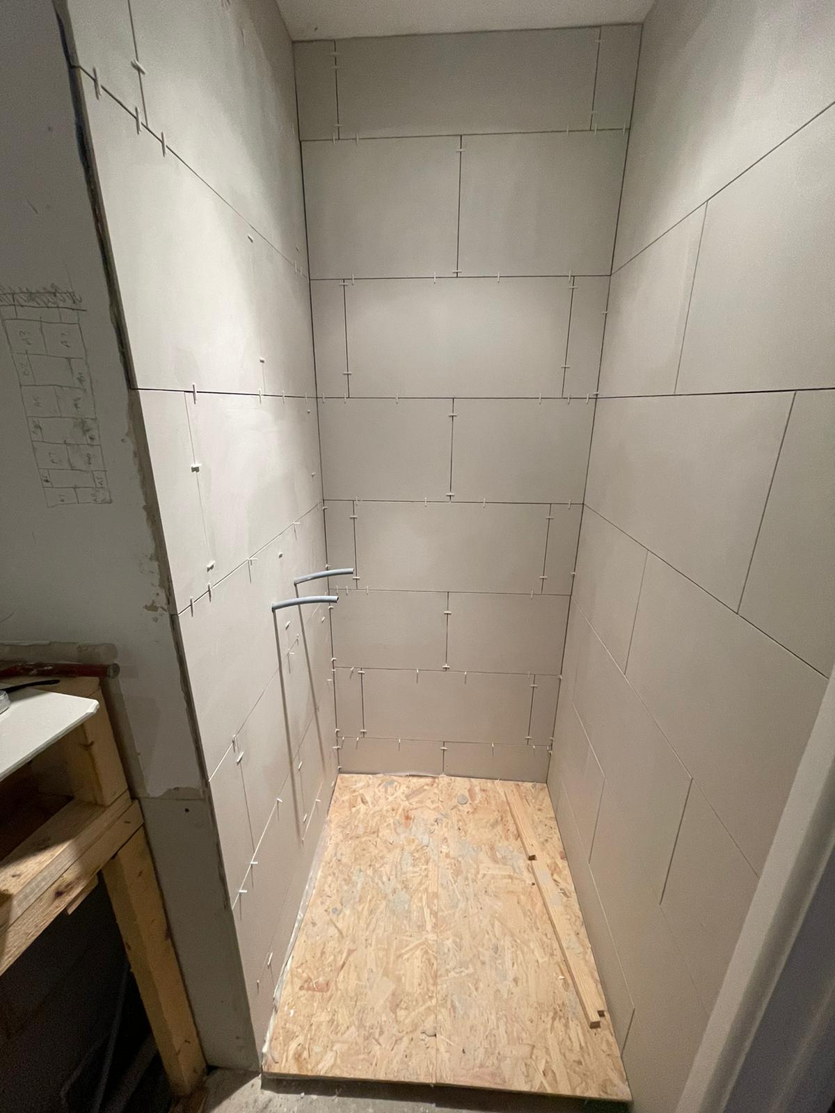Shower enclosure tiled Bare shower space with tiled walls and a wooden base, awaiting fixtures.