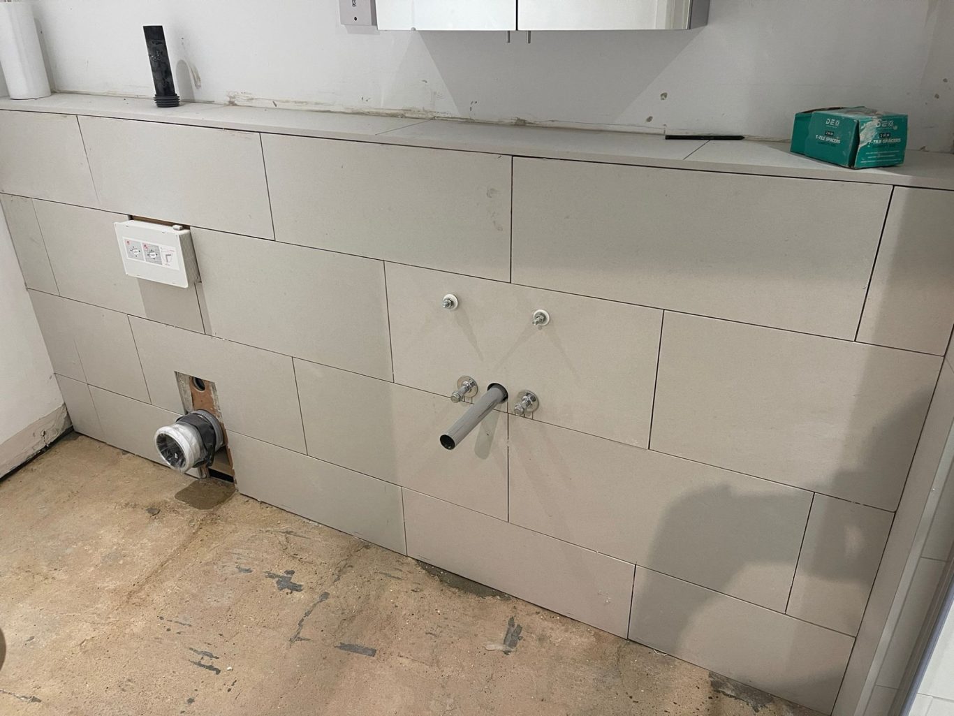 Bulkhead tiled Wall with tiled surface, water pipe fittings, and unfinished floor.