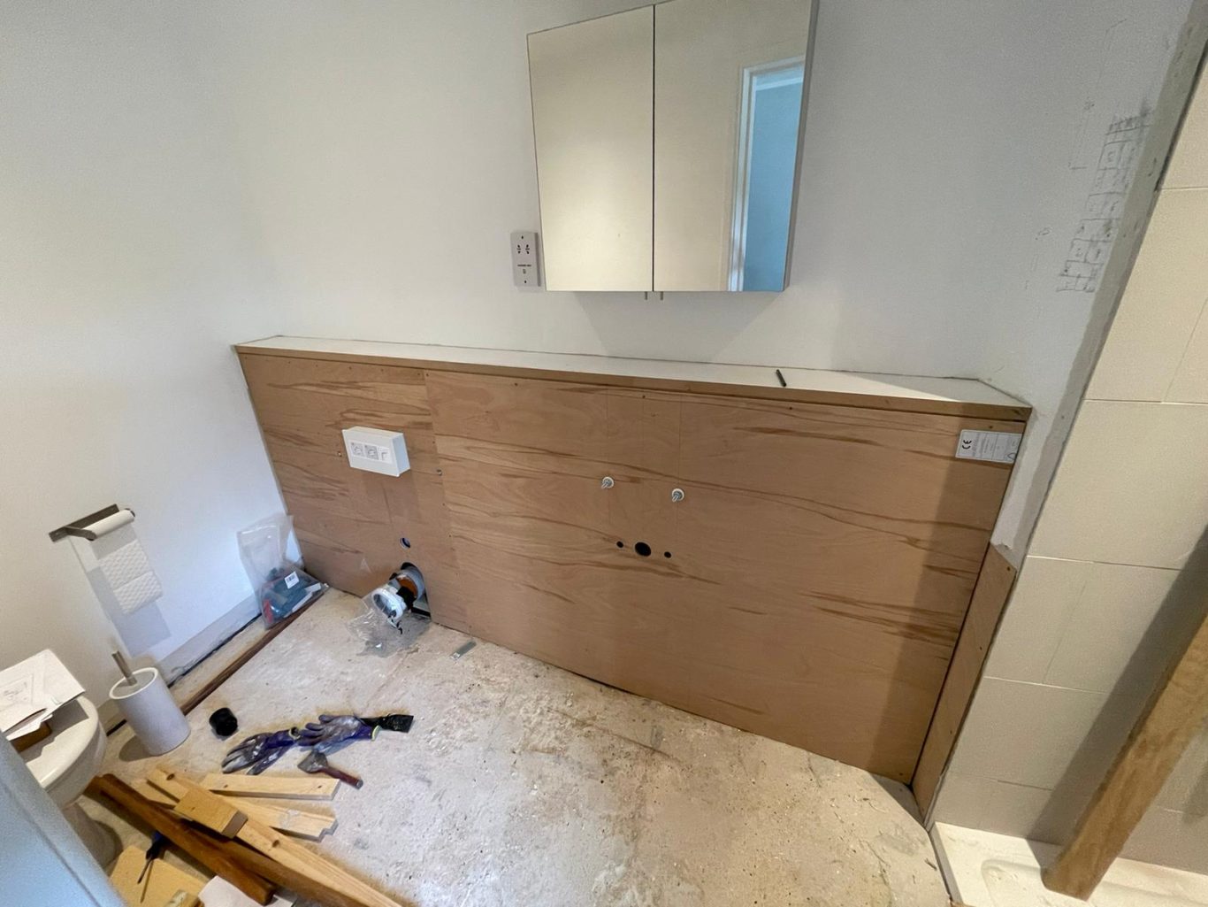 Bulkhead built ready for tiling Bathroom under construction with wooden panels, a mirror, and scattered tools.