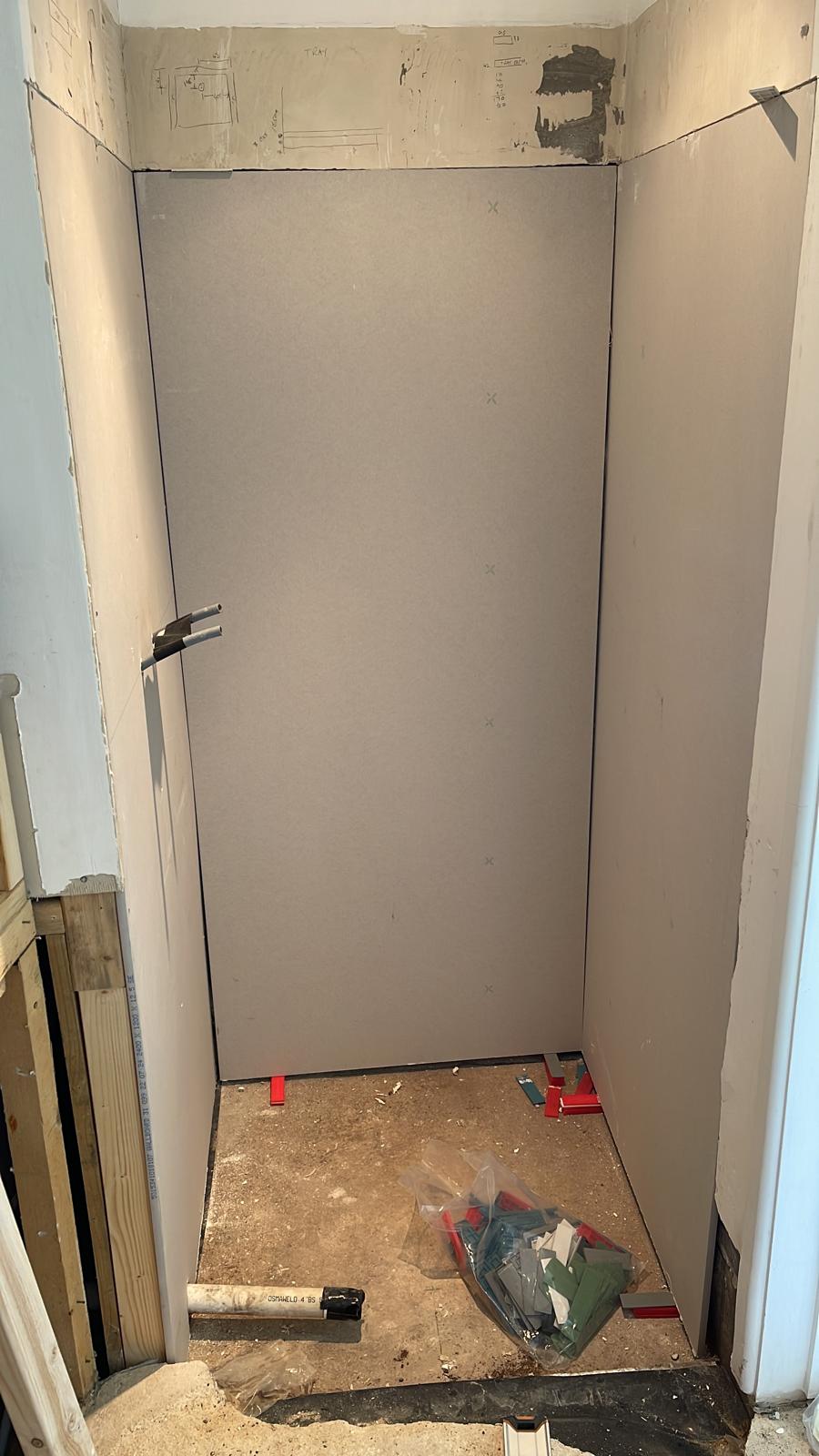 shower enclosure boarded out A grey partition in a room with tools and materials scattered on the floor.